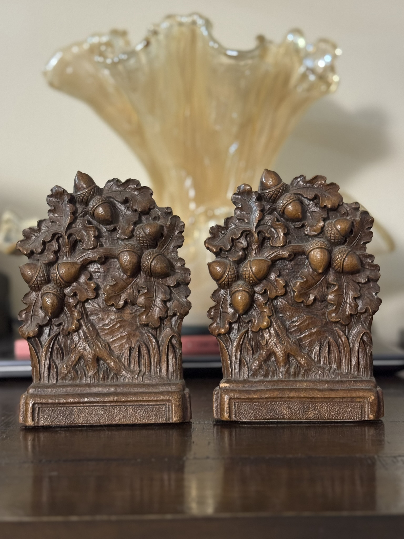 Two ornate bronze bookends with oak leaf and acorn detail sit on a wooden surface. Behind them is a Chinese Blue & White Miniature Vase, its elegant design recalling classic Chinese artistry.