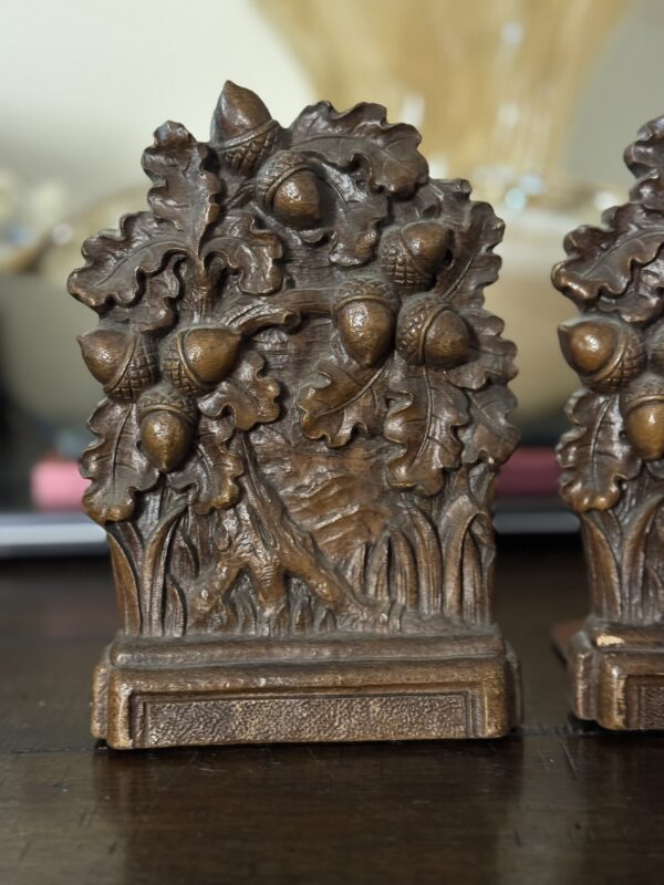 A detailed bronze-colored bookend with raised oak leaves and acorns features a rectangular, textured base. An intricate Chinese Blue & White Miniature Vase enhances the three-dimensional natural design, set against a softly blurred background.