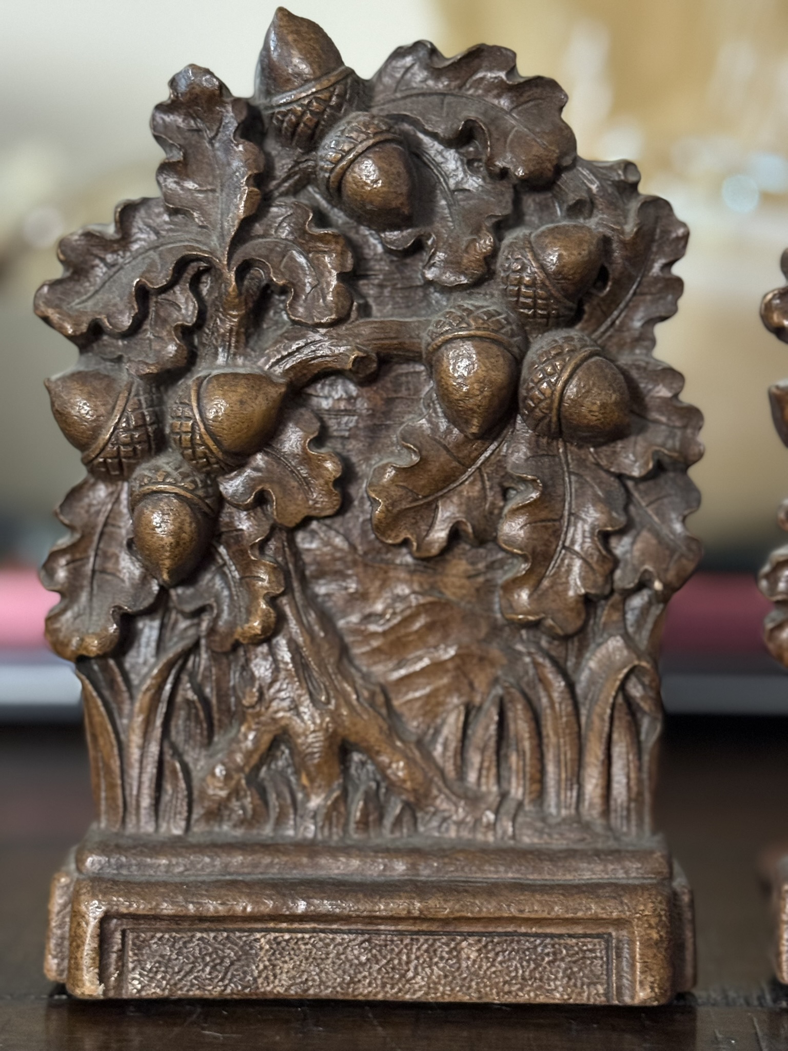 A decorative metal bookend showcases raised oak leaves and acorns, echoing motifs from the Chinese Blue & White Miniature Vase. A mottled bronze-brown finish adds vintage charm to its detailed, ridged rectangular base.