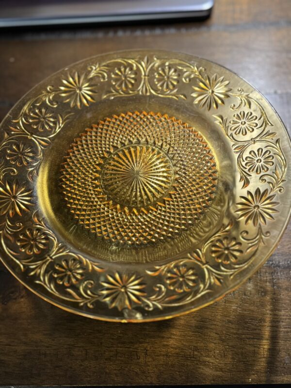 A Stangl Tulip Cup with intricate floral and geometric patterns and a raised, textured design in amber glass sits on a wooden surface, its vintage style catching the light beautifully.