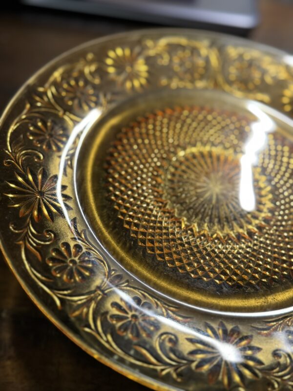 A close-up of the Stangl Tulip Cup, showcasing its round, amber-glass body with intricate floral and geometric patterns around the border and center. The glossy surface beautifully highlights every ornate detail reminiscent of classic Stangl designs.
