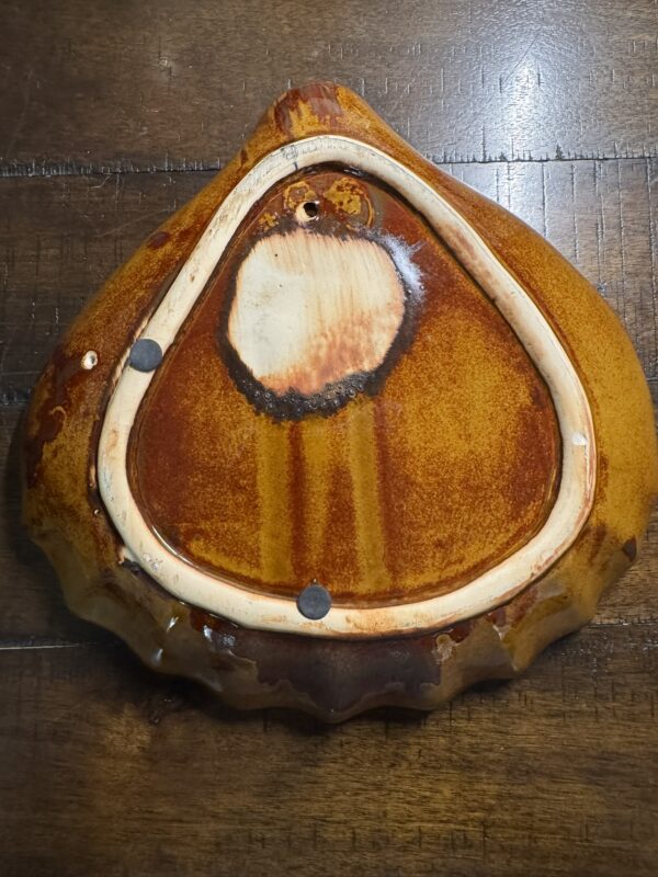 The image displays the underside of a glazed ceramic planter beside a Seashell Serving Tray, both placed on a wooden surface where metal pads and a drainage hole are visible.