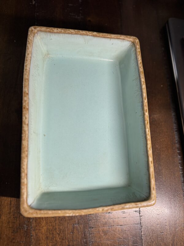 The Terracotta Bonsai Planter is a rectangular ceramic dish with a light blue interior and textured, light brown terracotta rim and exterior. It features slightly uneven edges for a handcrafted look and rests on a dark wooden surface.