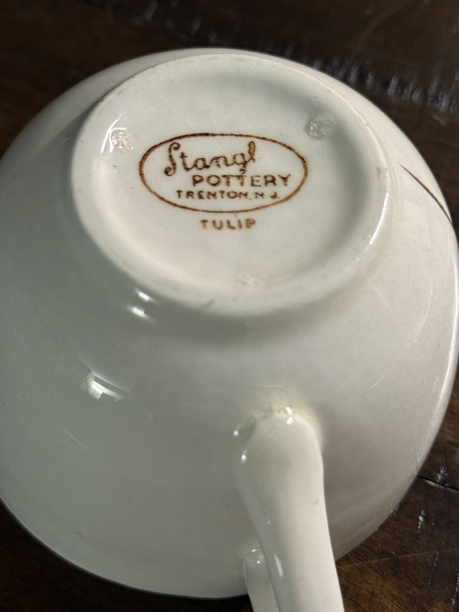 The underside of a Stangl Tulip Cup features the brown maker’s mark “Stangl Pottery Trenton, N.J. TULIP,” centered on the base, with the cup’s handle visible in the foreground.