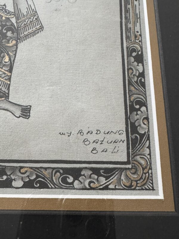 Close-up of a decorative artwork corner with intricate black and gold floral patterns on the border. In the lower right, handwritten text reads wy. Radung Batuan Bali. A part of a figures foot is visible on the left side.