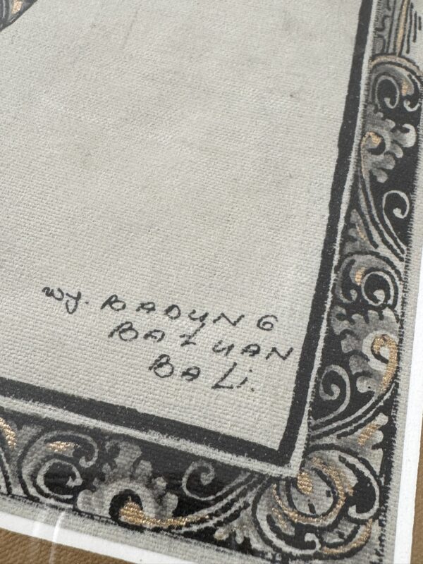 A close-up of the corner of a textured canvas features ornate black and gold patterns bordering the edge. Handwritten text in black ink reads, “W. Radjng Ratiyan Bali.” The canvas lies beneath a protective transparent sheet.