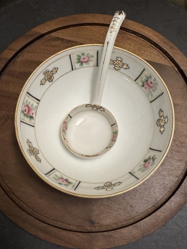 A decorative porcelain bowl with floral and yellow patterns along the rim sits on a round wooden board. A matching porcelain ladle rests inside the bowl, its handle patterned and slightly worn at the tip.