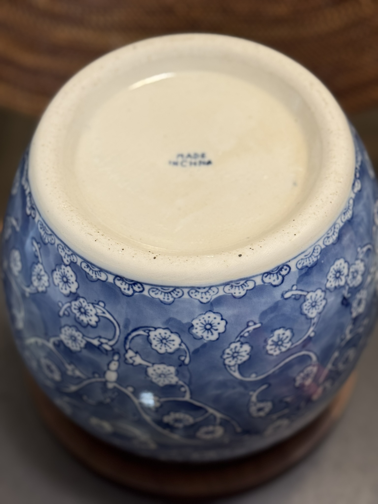 A blue and white ceramic vase is shown upside down, displaying its base. The vase features a floral pattern with white blossoms on blue. The bottom is unglazed except for the center, which has the text MADE IN CHINA stamped in blue.