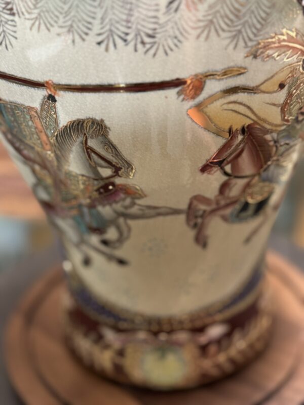 A close-up of a decorative vase featuring an intricate painted scene of two armored knights on horseback jousting, with lances extended. The design is detailed and colorful, set against a glossy ceramic background.