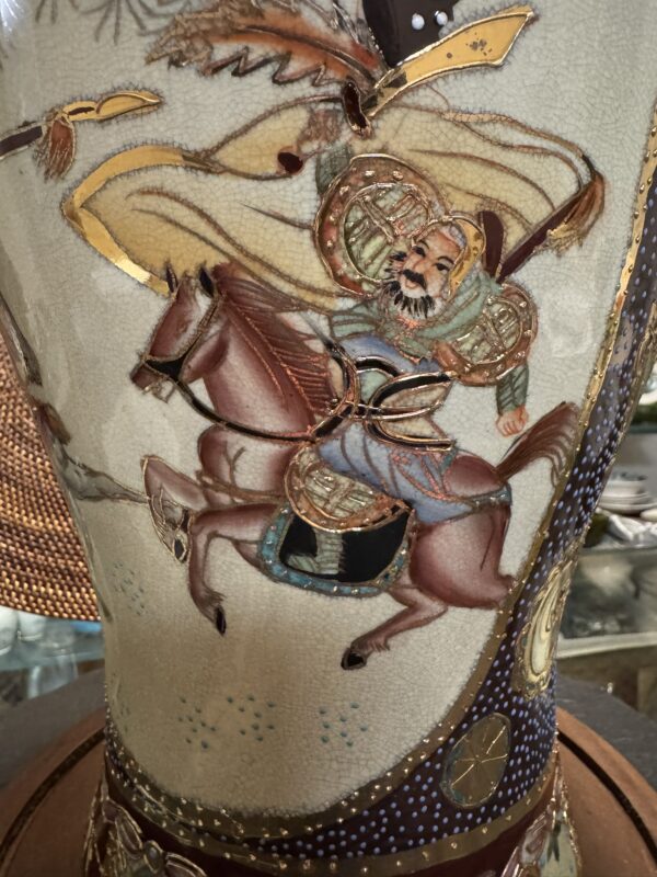 A detailed painting on a vase shows an armored warrior with a beard, riding a brown horse. The warrior wears ornate armor and holds a weapon, with a flowing yellow banner behind him. The scene is richly decorated with gold accents and intricate patterns.