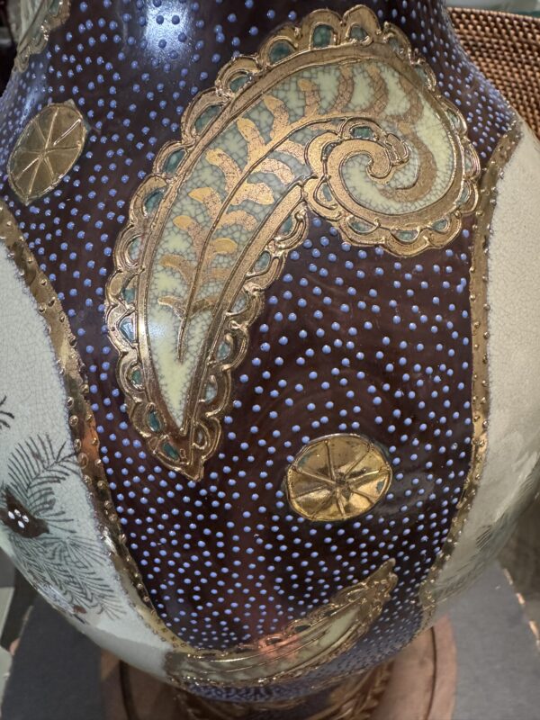 A close-up of a ceramic vase features a decorative paisley pattern in gold, green, and tan on a dark brown background with white raised dots and gold circular motifs, highlighting intricate textures and glossy surface details.