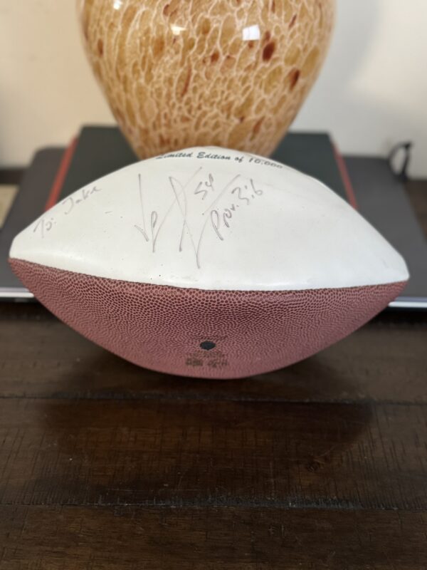 A Jeremiah Trotter, Sr. Philadelphia Eagles Football with a white signed panel and “Prov. 3:6,” marked “Limited Edition of 10708,” sits on a wooden table near a brown vase and closed book.