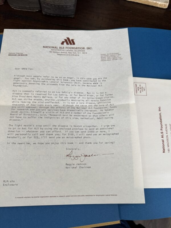A typed letter from the National ALS Foundation, signed by Reggie Jackson, sits on a blue folder. The letter addresses the reader about ALS awareness and fundraising. Next to it is a matching envelope with the foundation’s name and address. The items are on a wooden table.
