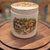 A ceramic jar with a colorful, detailed scene depicting people, horses, and dogs in front of a cottage. The jar has a matching lid, and both sit on a round wooden board with blurred chairs and objects in the background.