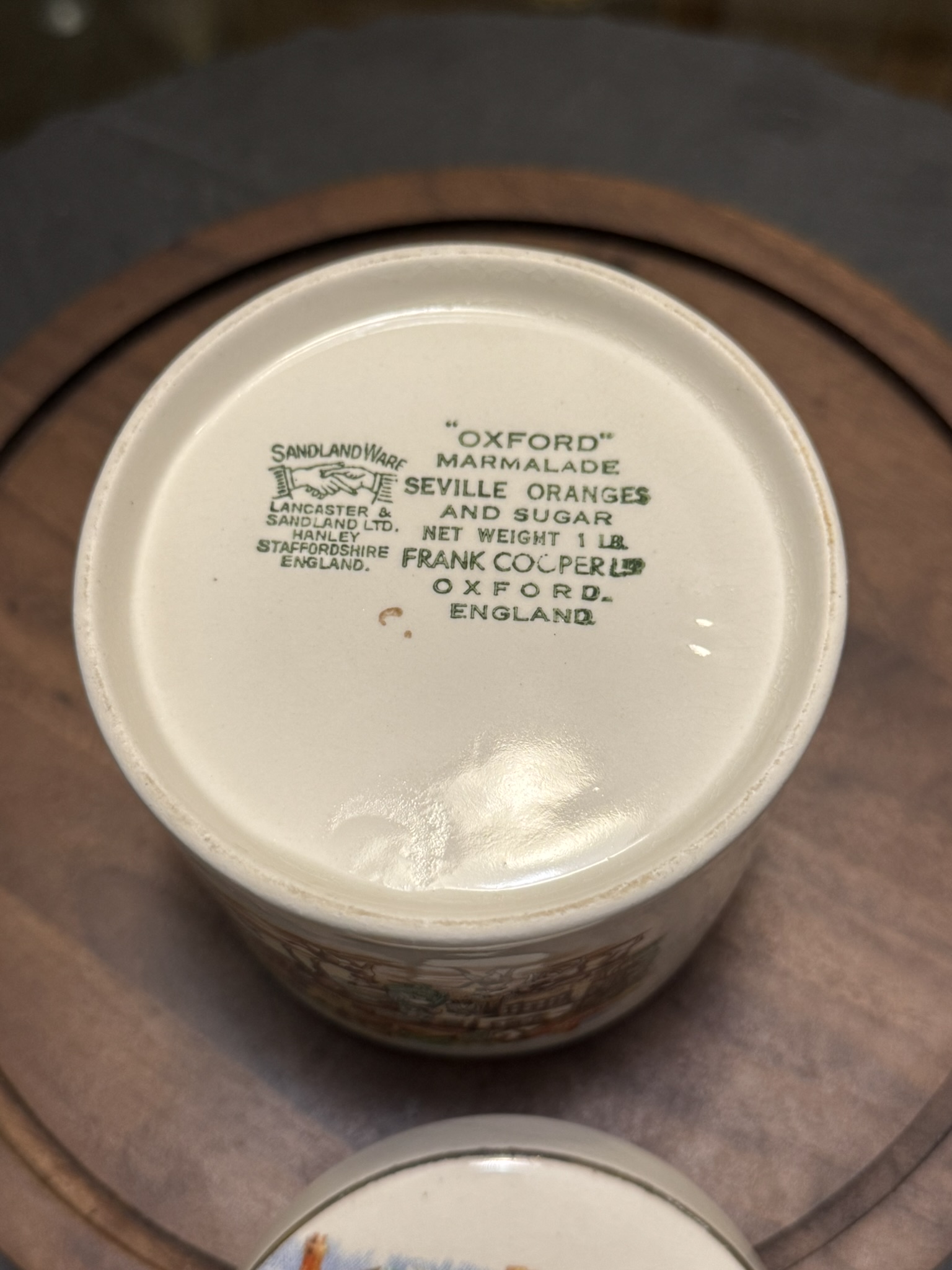 The bottom of a ceramic jar displays green text reading: “Oxford Marmalade, finest Seville oranges and sugar, net weight 1 lb, Frank Cooper Ltd, Oxford, England.” The Sandland Ware maker’s mark and Lancaster & Sandland Ltd, Hanley, Staffordshire, England are also visible.