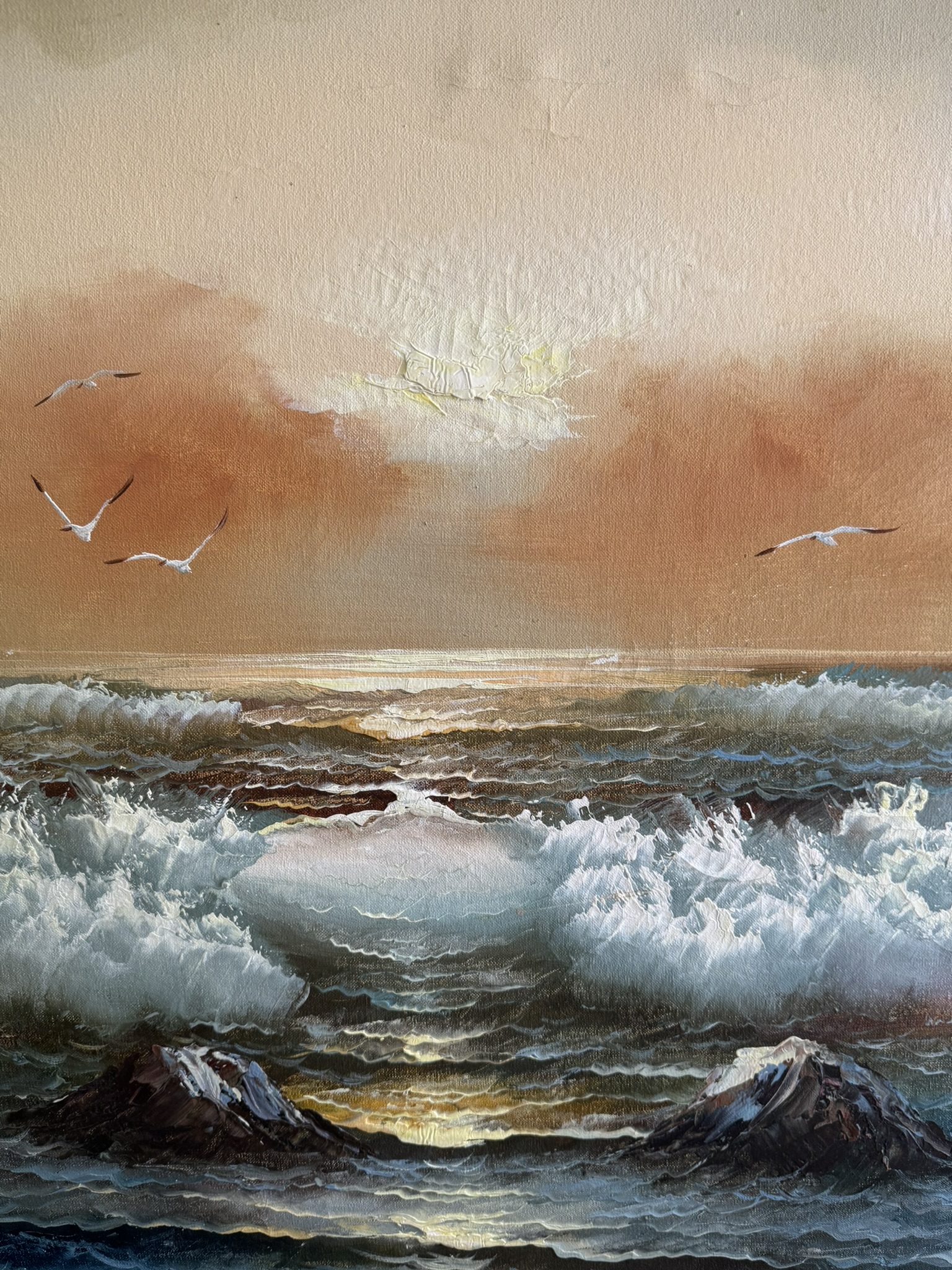 A seascape painting depicts crashing waves under a warm orange sky at sunset. Four seagulls soar above the water, with sunlight glinting off the sea. Rocky outcrops emerge from the surf in the foreground, while wispy clouds float near the horizon.