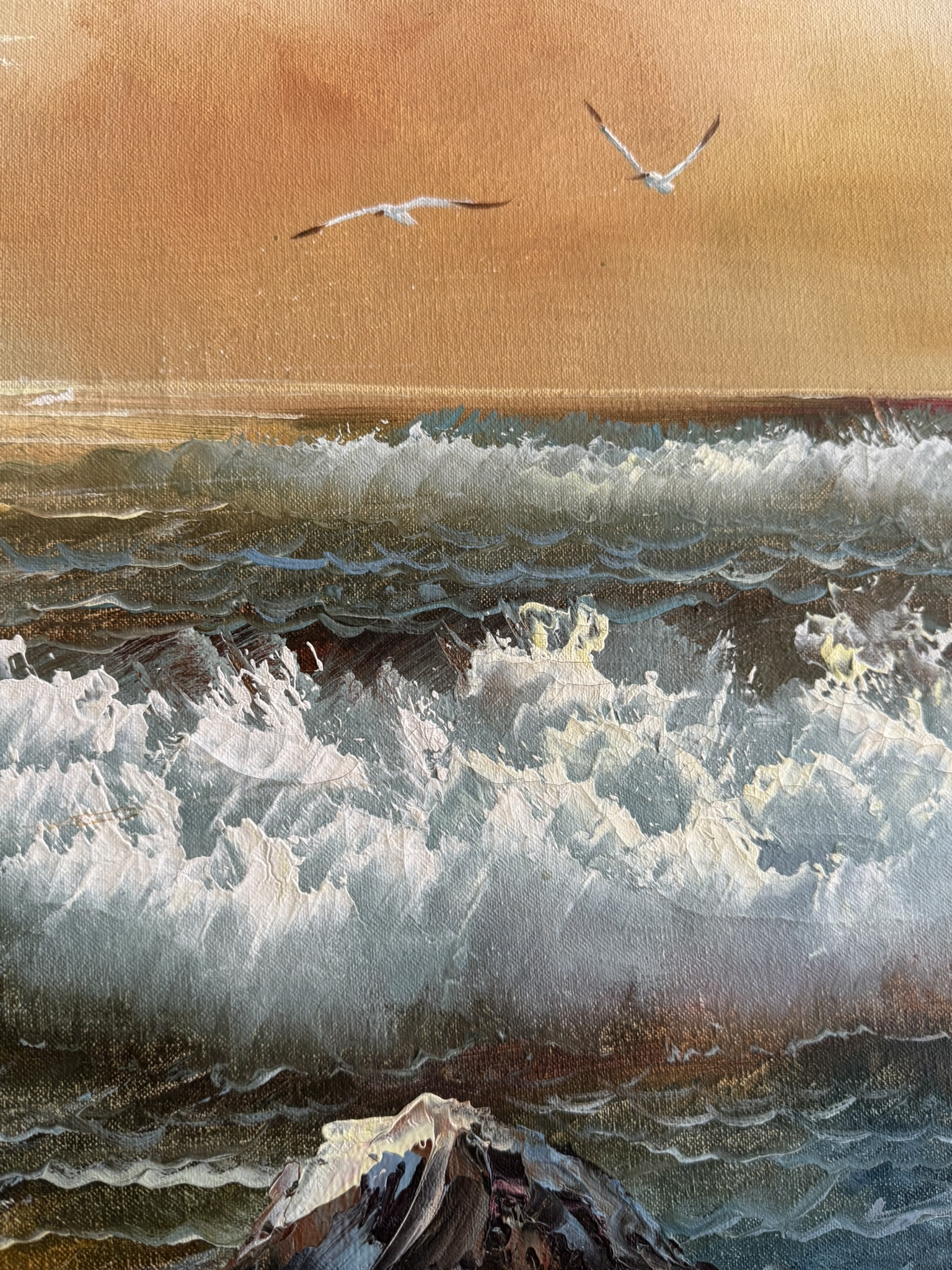 A painting depicts crashing ocean waves under an orange sky at sunset. Two seagulls soar in the distance above the horizon. The textured brushstrokes capture the foamy water and dynamic movement of the sea. A dark rock is visible in the foreground.