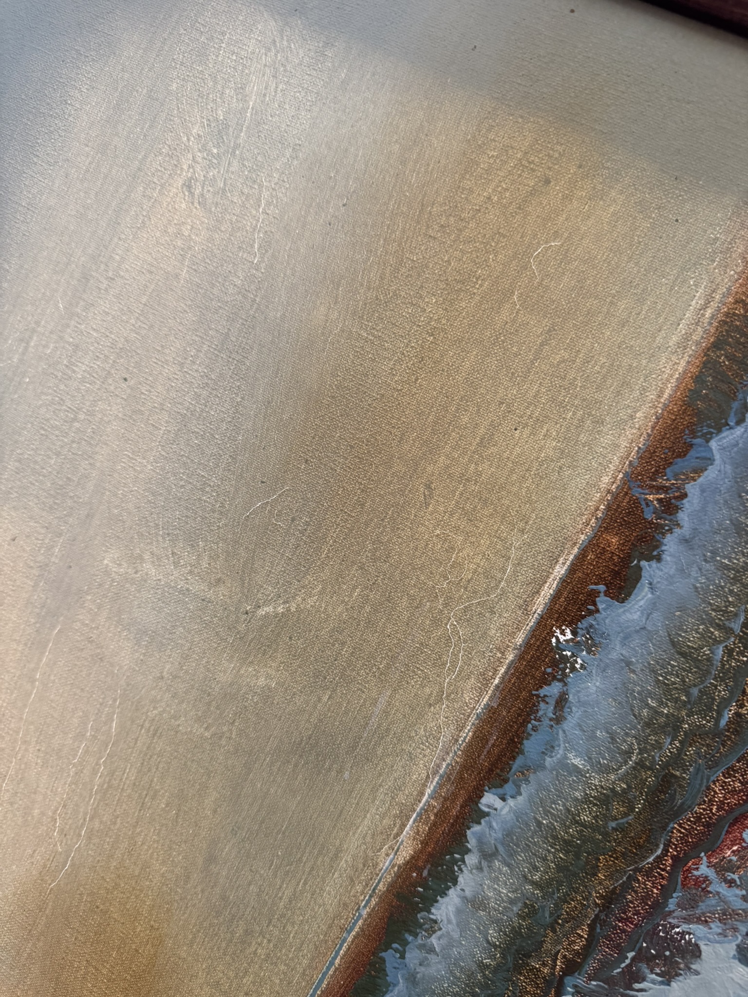 A close-up of a textured surface featuring a smooth, metallic gold area with subtle brushstrokes. In the lower right, theres a border of rough, rust-colored and blue-gray textures resembling waves or corrosion along the edge.