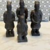 Four small dark statues of ancient Chinese terracotta warriors, three standing and one kneeling, are arranged on a light marble surface. The background has blue and white geometric tiles with an interlocking pattern.