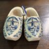 The Wooden Delft Clogs feature hand-painted blue windmills, houses, and trees in traditional Dutch style. A blue and white ribbon connects the decorative clogs, making them a charming addition to any surface.