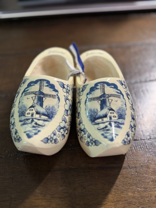 The Wooden Delft Clogs feature hand-painted blue windmills, houses, and trees in traditional Dutch style. A blue and white ribbon connects the decorative clogs, making them a charming addition to any surface.
