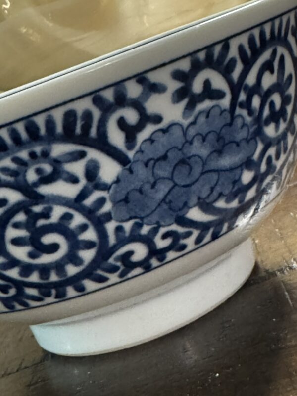 A close-up of the Tako Karakusa Bowl, highlighting its blue and white floral and vine patterns along the rim with a cloud motif among swirling lines, set on a wooden surface.
