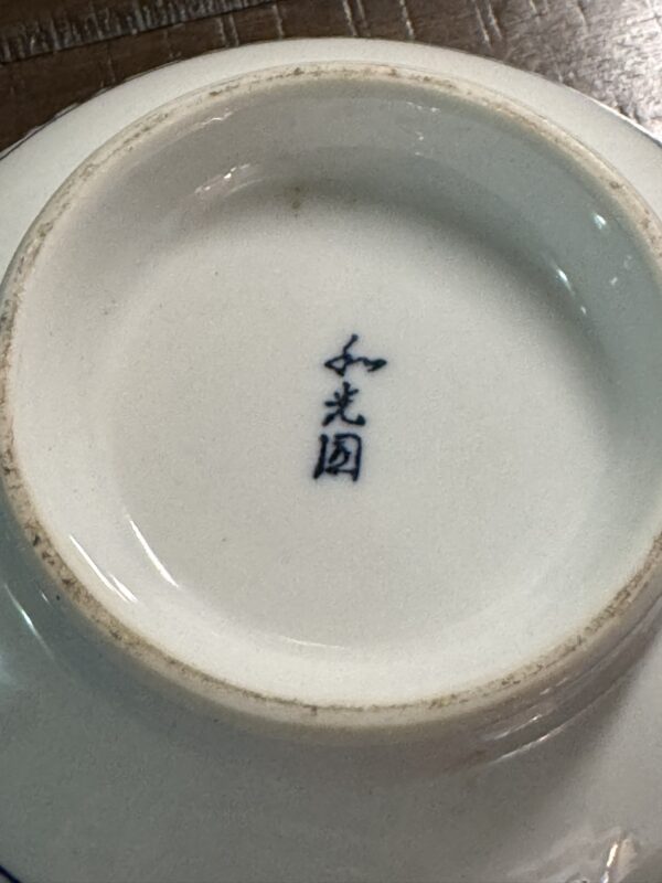The image displays the bottom of the Tako Karakusa Bowl, featuring a central blue four-character Chinese mark. The unglazed base ring has some discoloration, while the surrounding white porcelain is smooth and glossy.